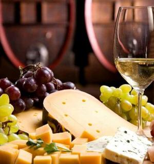 a glass of wine next to a bunch of cheese and grapes