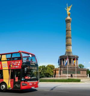a red double decker bus driving past a statue
