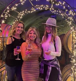 three women holding wine glasses in front of a barrel