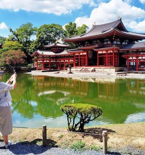 a woman taking a picture of a building in front of a pond