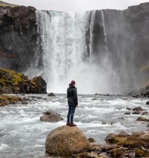 osoba stojící na skále před vodopádem