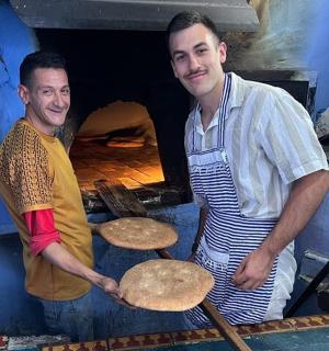 two men standing in a kitchen with two pizzas