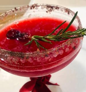 a red drink in a glass with a rosemary garnishment