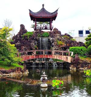 a bridge over a pond in a park with a fountain