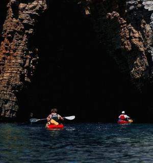 两个人在洞穴附近的水中划皮艇