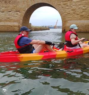 two people in a kayak in the water under a bridge