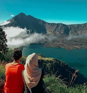 two people sitting on top of a mountain overlooking a lake