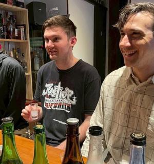 三个男人围着桌子站着，桌子上摆满了酒瓶