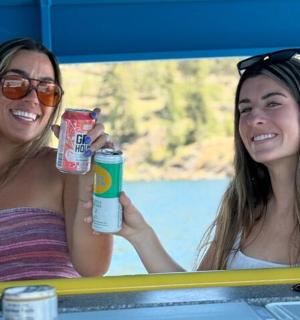 dwie kobiety siedzące przy stole i trzymające w rękach napoje