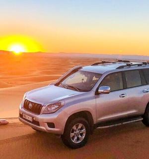a suv in the desert with the sunset in the background