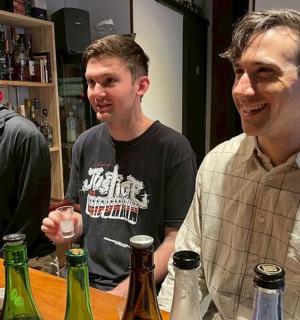 三个男人站在酒吧周围，手里拿着几瓶酒