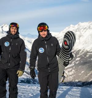 两个男人站在雪地里，手里拿着滑雪板