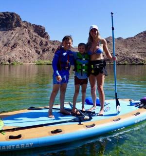 žena a dvě děti stojící na paddleboardu ve vodě