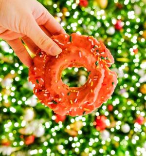 a person holding a donut in front of a christmas tree