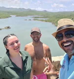 a group of three men standing in front of a lake