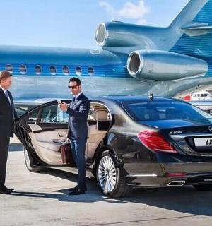 two men in suits standing next to a car at an airport