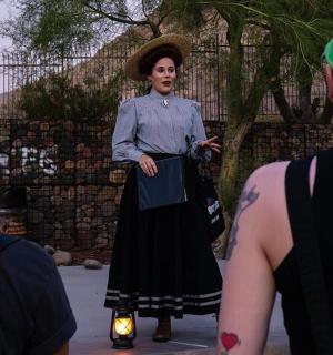 žena v šatech a klobouku mluvící s lidmi