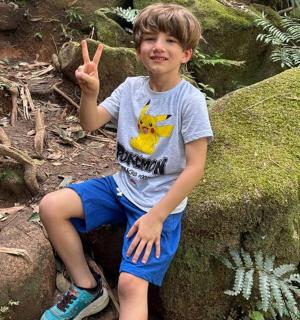 a young boy sitting on a rock giving the peace sign