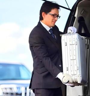 一名穿着西装、提着行李箱站在汽车旁边的男子