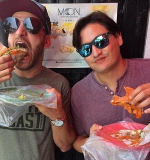 two men eating food while standing next to each other