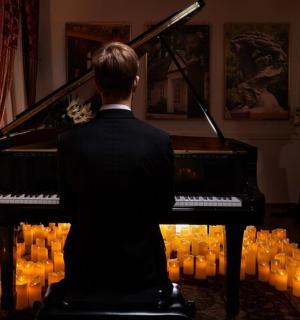 一名男子坐在钢琴前,点着蜡烛