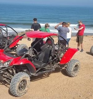 Skupina lidí stojící na pláži se čtyřmi čtyřkolkami