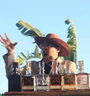 a man in a hat standing behind a table with bottles