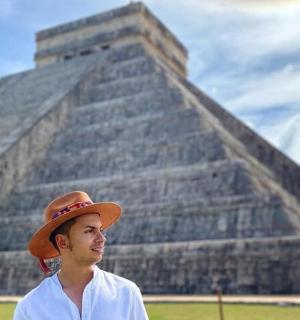 a man wearing a hat standing in front of a pyramid