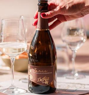 una persona che apre una bottiglia di vino su un tavolo con dei bicchieri