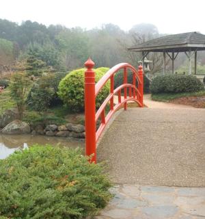 a red bridge over a river in a garden