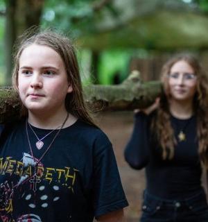 two girls and a boy carrying a log in the woods