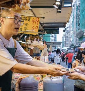 一名男子站在市场里，周围有人拿着手机