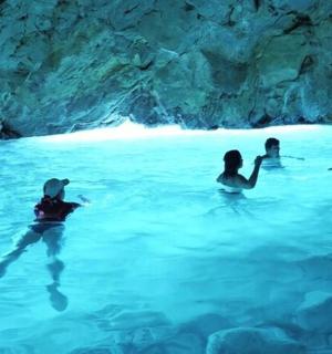 a group of people swimming in a blue cave