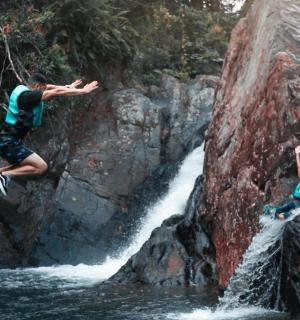 two people jumping off a rock into a waterfall