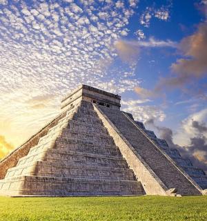 a pyramid in a field with a cloudy sky