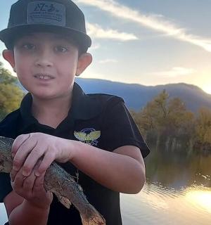 a boy holding a fish in his hands on a lake