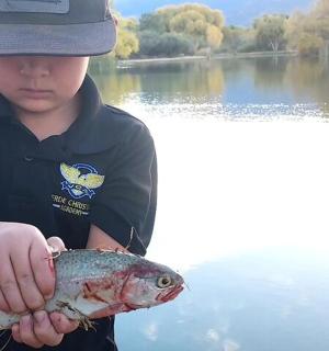 a boy holding a fish in his hands on a lake