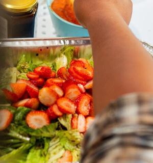 a person is reaching into a salad with strawberries