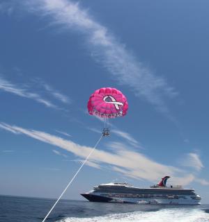 eine Person, die einen rosa Drachen über einem Kreuzfahrtschiff steigen lässt