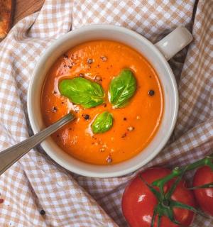 桌上有一碗汤、一把勺子和西红柿