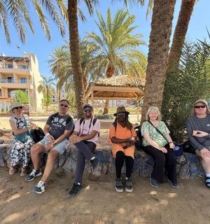 a group of people sitting on a stone bench under palm trees