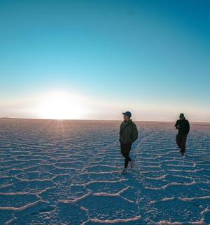 three men walking in the desert with the sun in the background