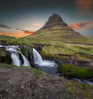 a waterfall in front of a hill with a mountain