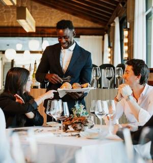 skupina lidí sedících kolem stolu s číšníkem