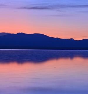 a sunset over the water with mountains in the background
