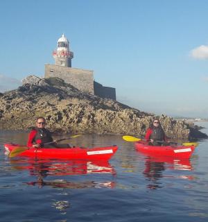 两个人划着皮划艇在水面上，远处有一座灯塔。