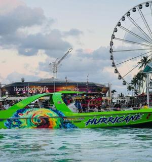 a green boat in the water next to a ferris wheel