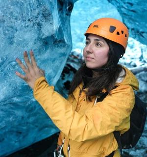 Eine Frau mit orangefarbenem Helm steht neben einem Gletscher