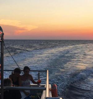 skupina lidí jedoucích na lodi při západu slunce