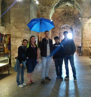 група људи стоји под плавим кишобраном